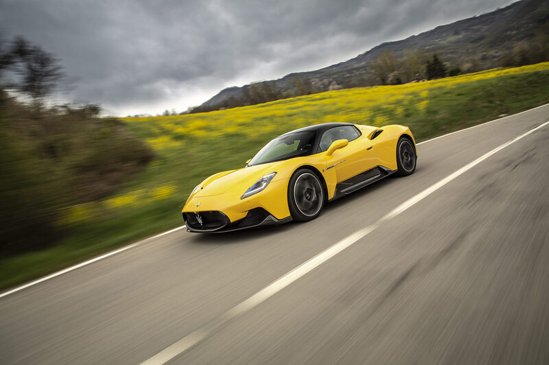 Maserati MC20 in yellow, front three-quarter on a country road beneath a rape-seed field